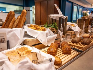Une variété de pains et de viennoiseries présentés sur une planche en bois, dans un cadre d’hôtel.