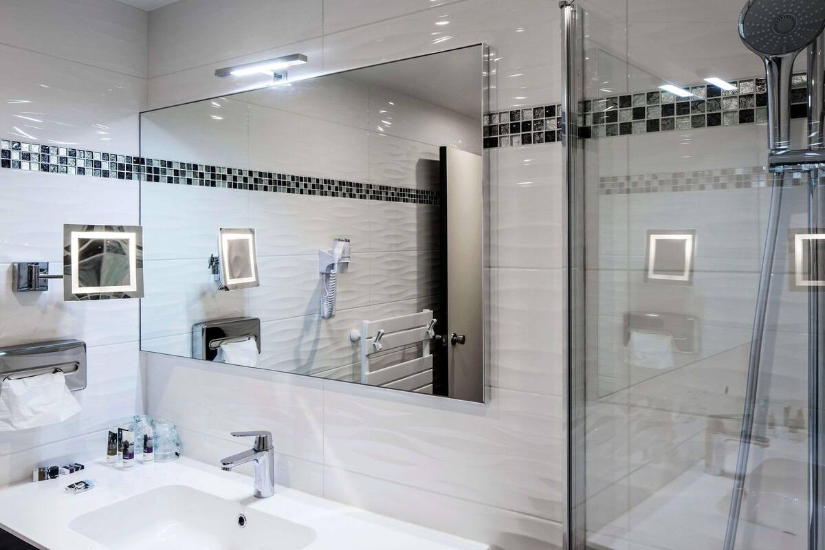 Une salle de bain moderne avec un grand miroir, une douche en verre et un lavabo blanc.
