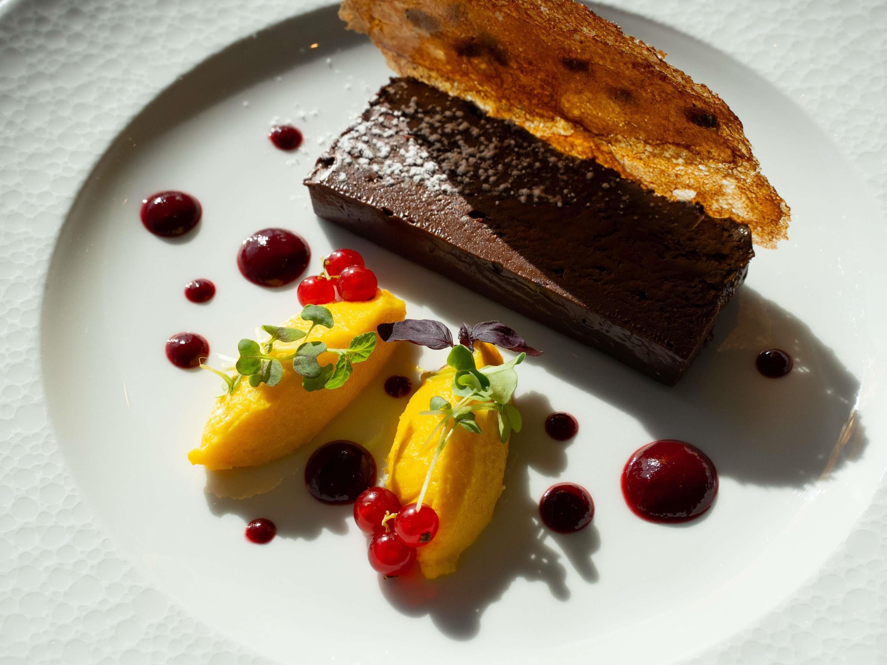 Une assiette de dessert avec un morceau de chocolat, deux éléments jaunes et des baies rouges.