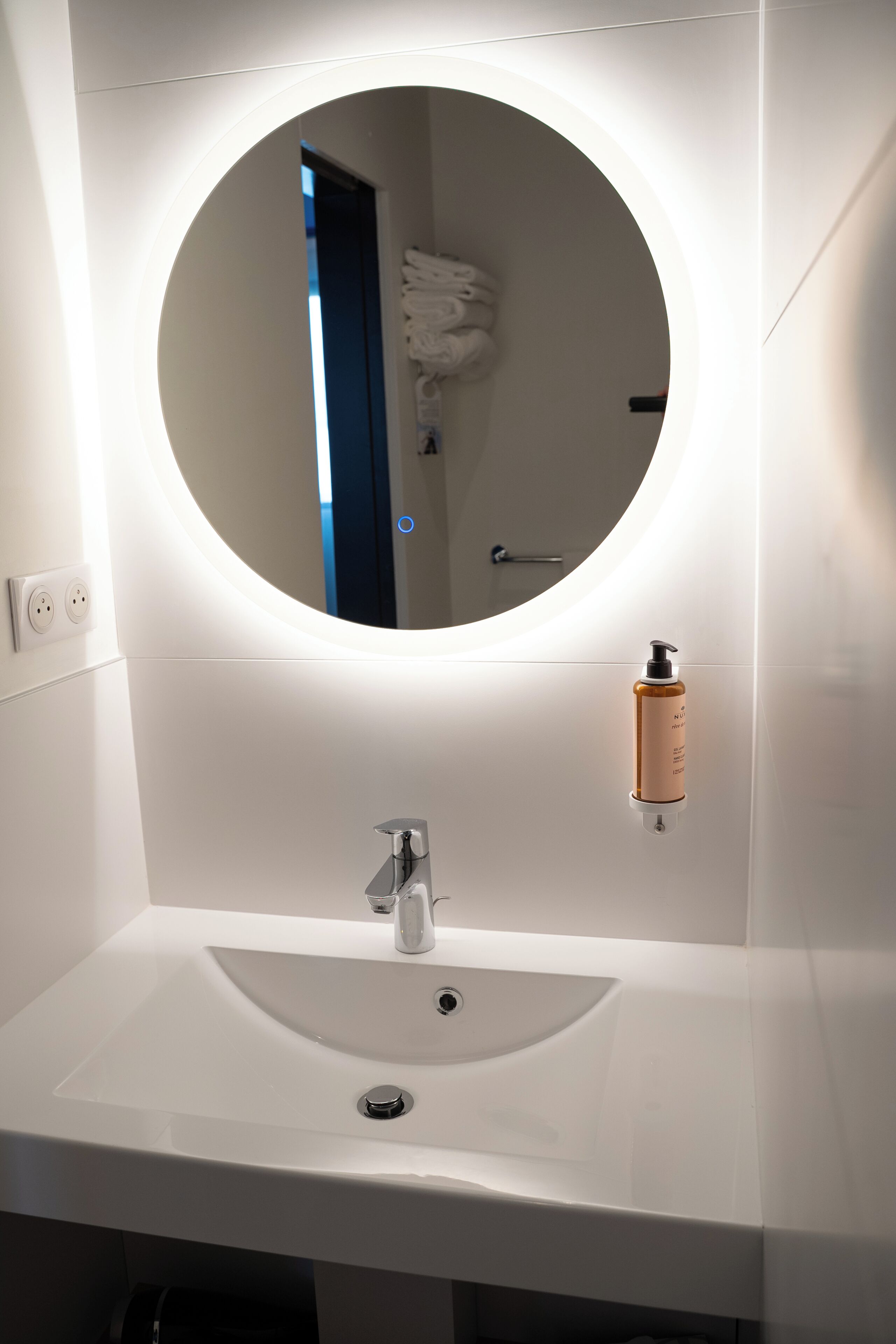 A bathroom with a round mirror, a white sink, and a soap dispenser.
