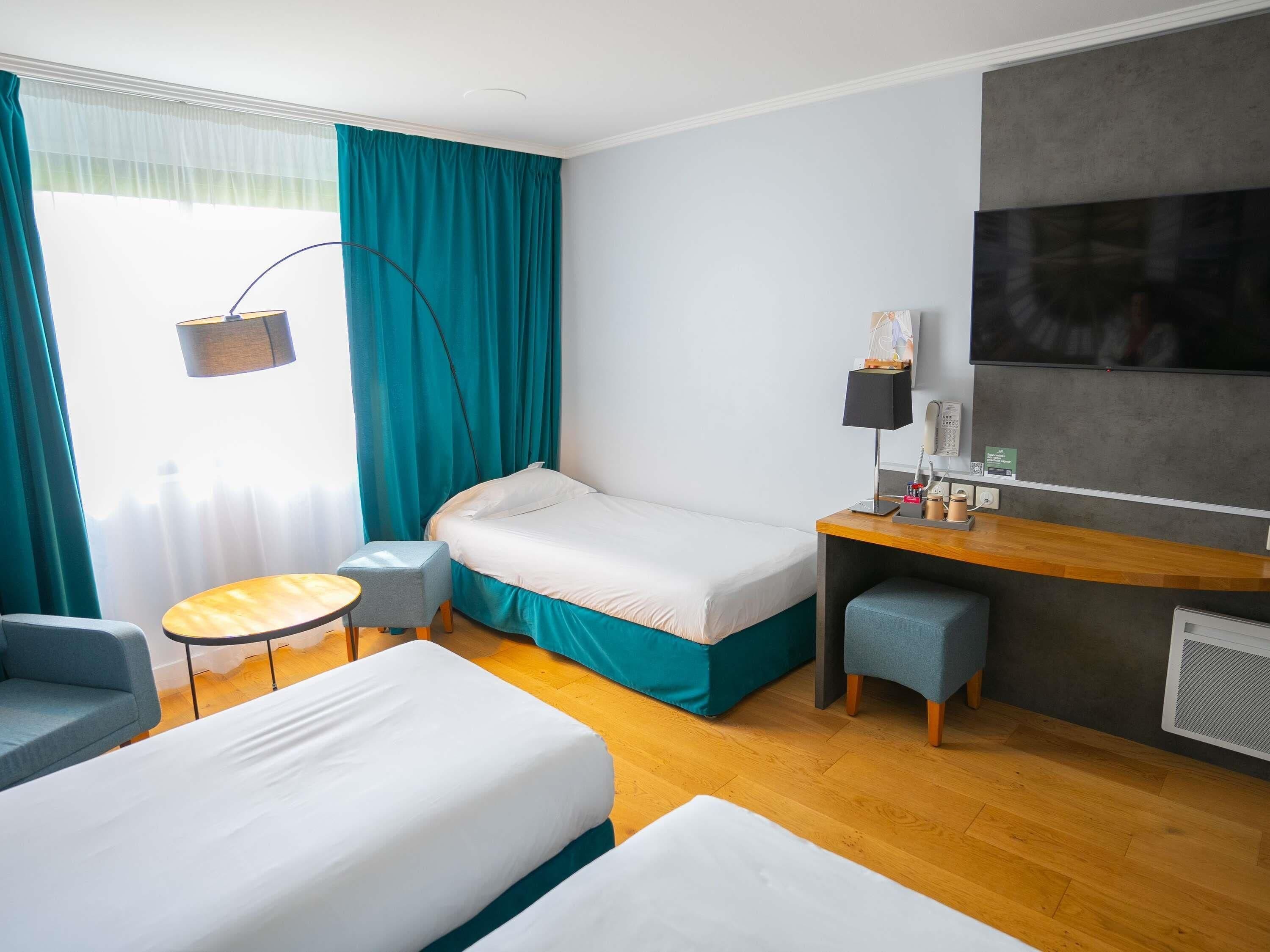 A hotel room with a bed, a desk, a chair, a small table, and a TV.