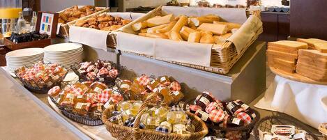 Un bufé con diversos alimentos, incluyendo pan, pasteles y salsas.