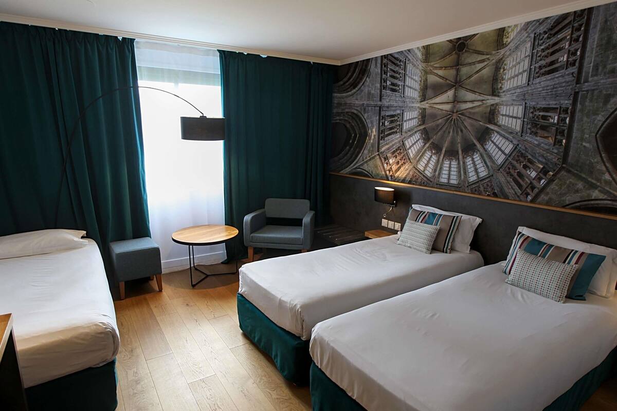 Une chambre d’hôtel avec deux lits, une petite table, une chaise et une grande fresque murale.