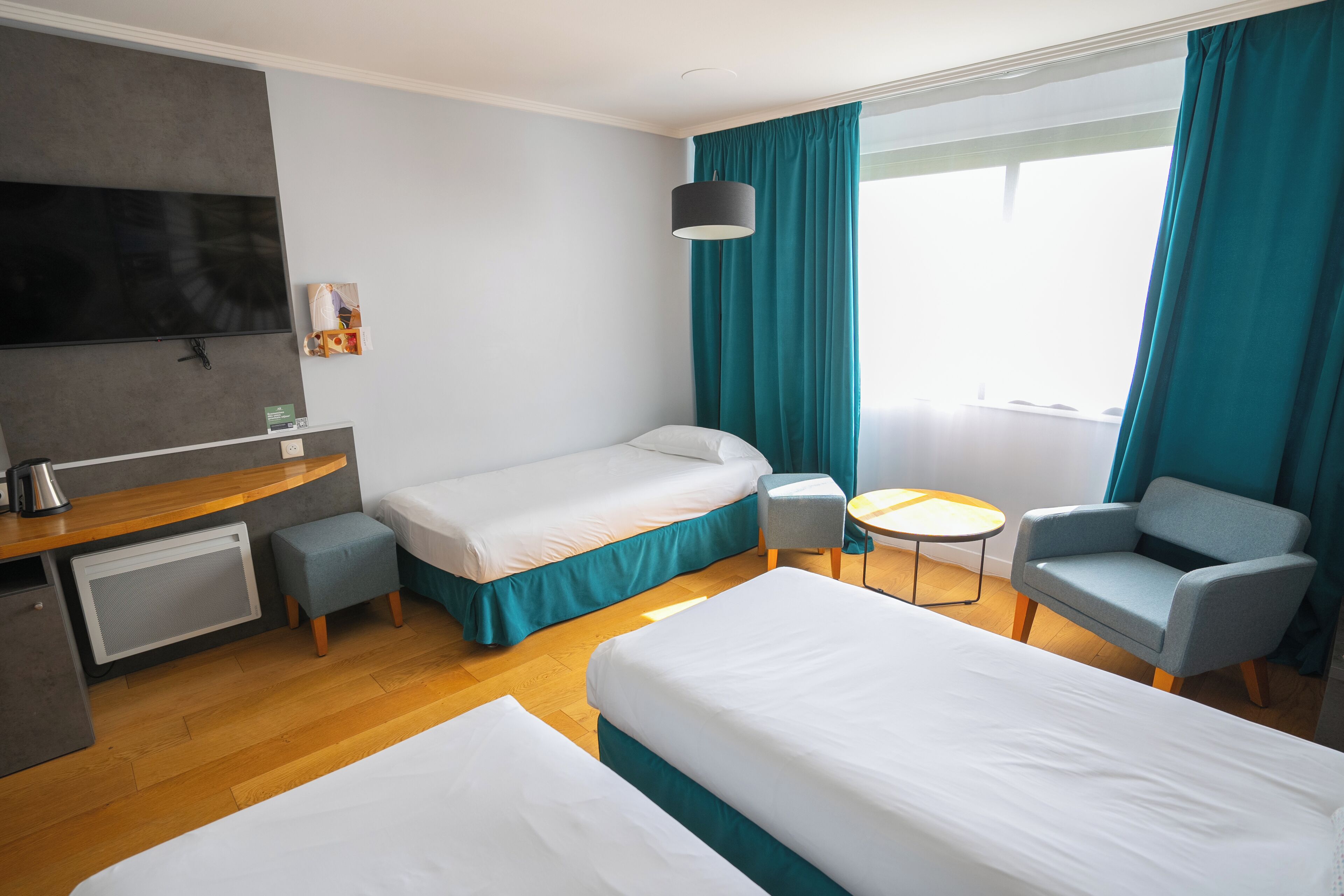 A hotel room with two beds, a desk, a chair, a TV, and a window with curtains.