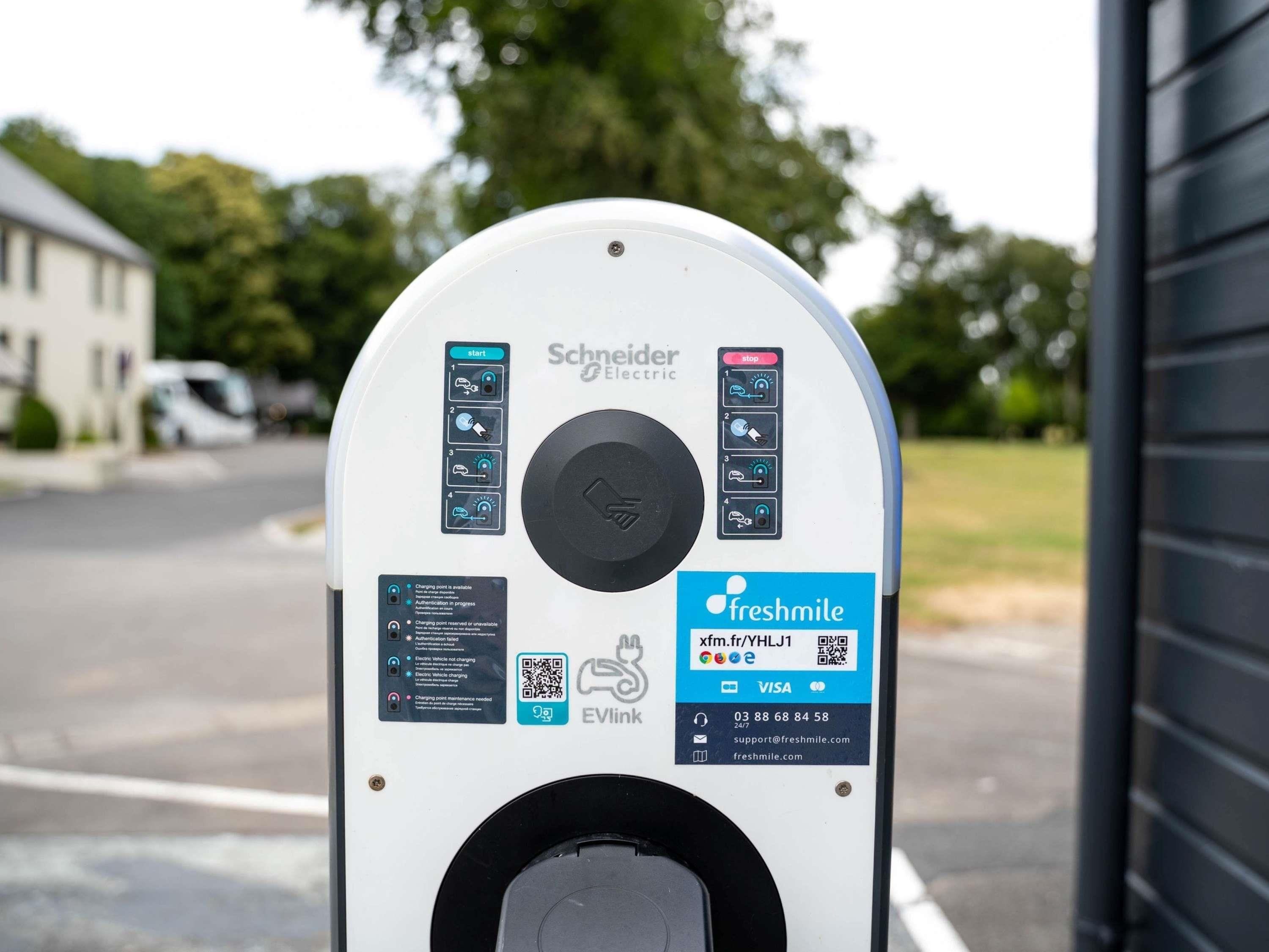 A white electric vehicle charging station with a QR code, a charging point availability indicator, and a Freshmile logo.
