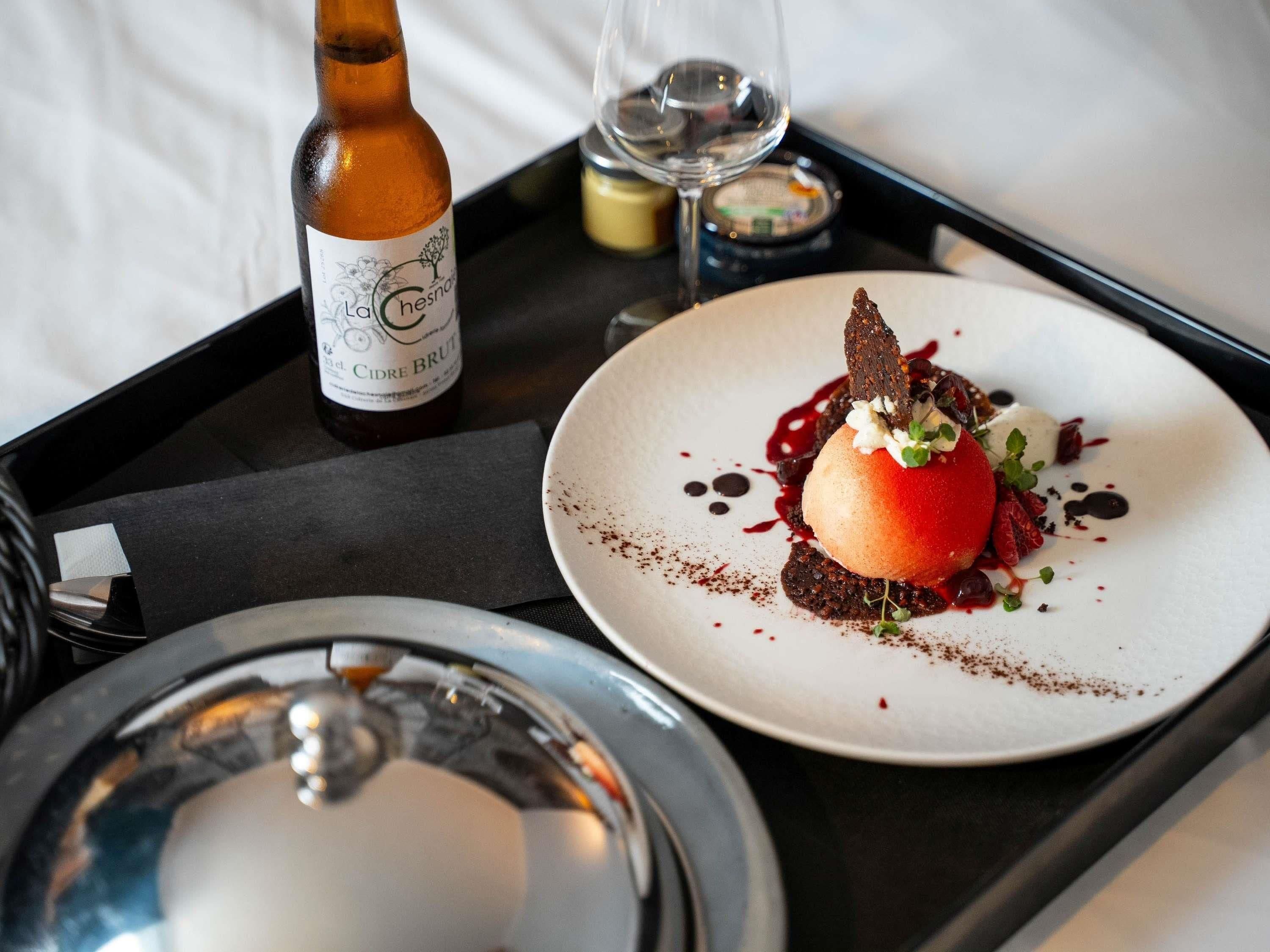 A dessert plate with a chocolate dessert, a bottle of Cidre Brut, and a glass of white wine on a tray.