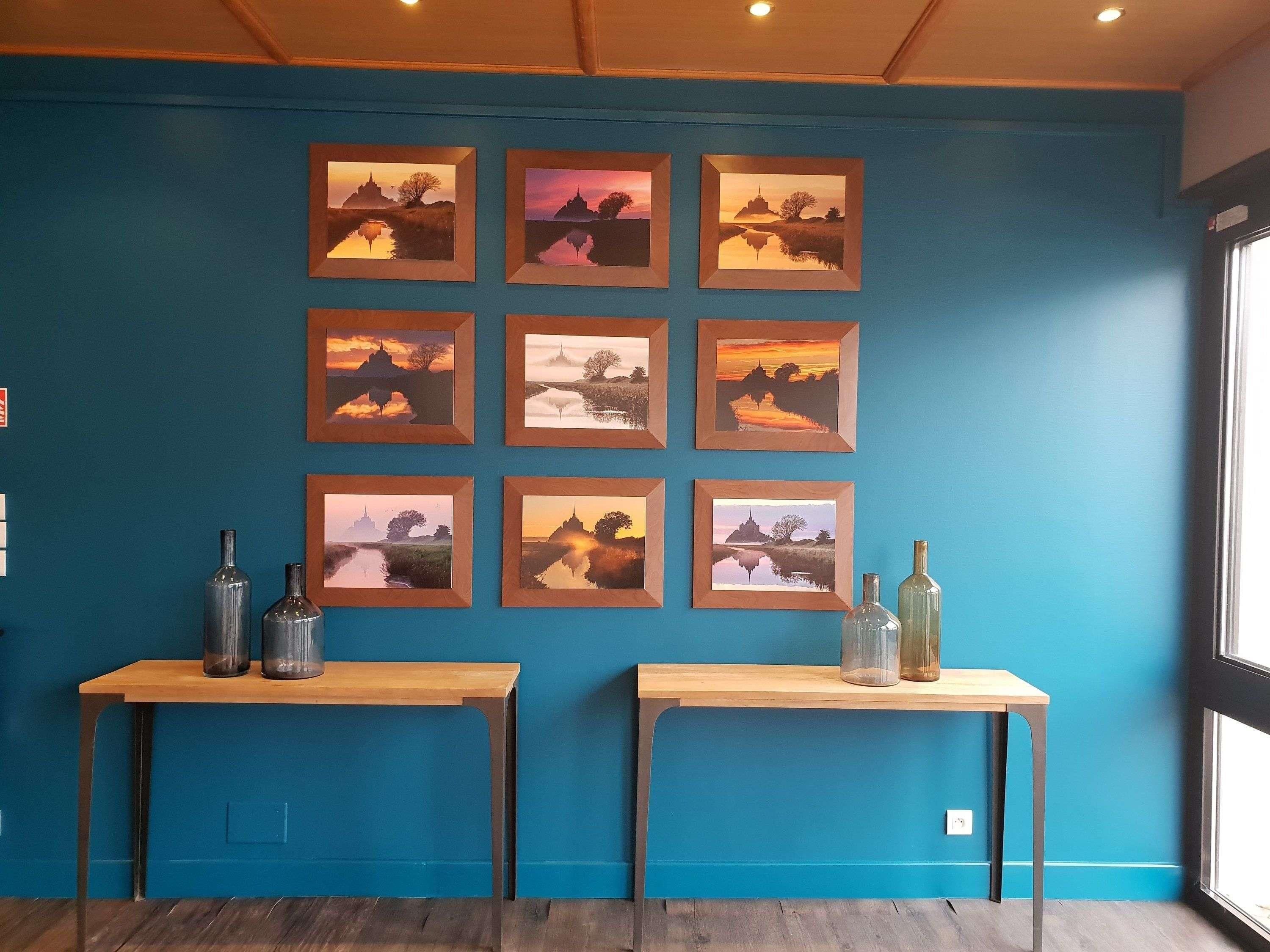 Una habitación con pared azul, mesas de madera y cuadros con paisajes.