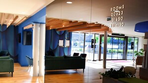 Un hall d’hôtel moderne avec un plancher en bois, des canapés verts et une cloison en verre.