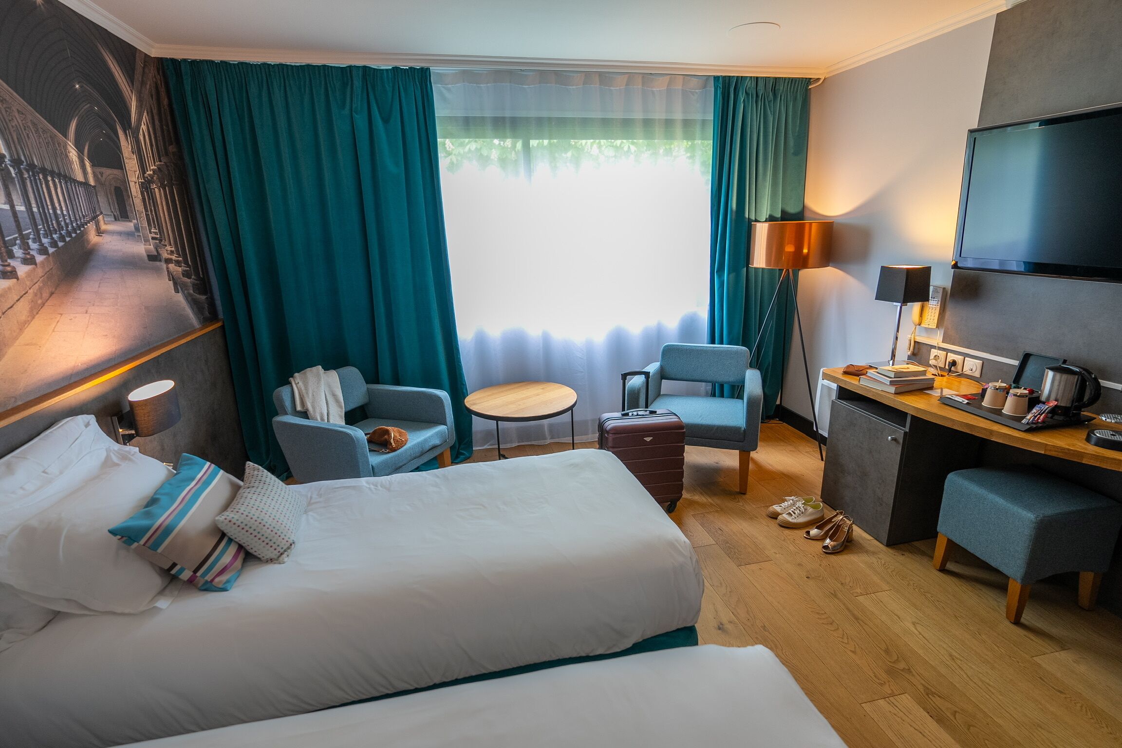 Een hotelkamer met een groot bed, een bureau, een stoel, een klein tafeltje en een televisie.