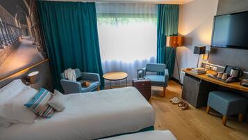 Een hotelkamer met een groot bed, een bureau, een stoel, een klein tafeltje en een televisie.
