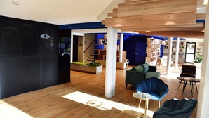Un intérieur moderne avec un plancher en bois, un escalier, un espace de vie comprenant un canapé et des fauteuils, ainsi qu’une bibliothèque.