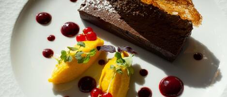 A dessert plate with a chocolate piece, two yellow items garnished with red berries and greenery, and a piece of bread.