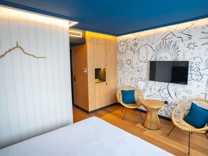 Een hotelkamer met een bed, twee rieten stoelen, een televisie en een muur met een decoratief muurdecoratie.