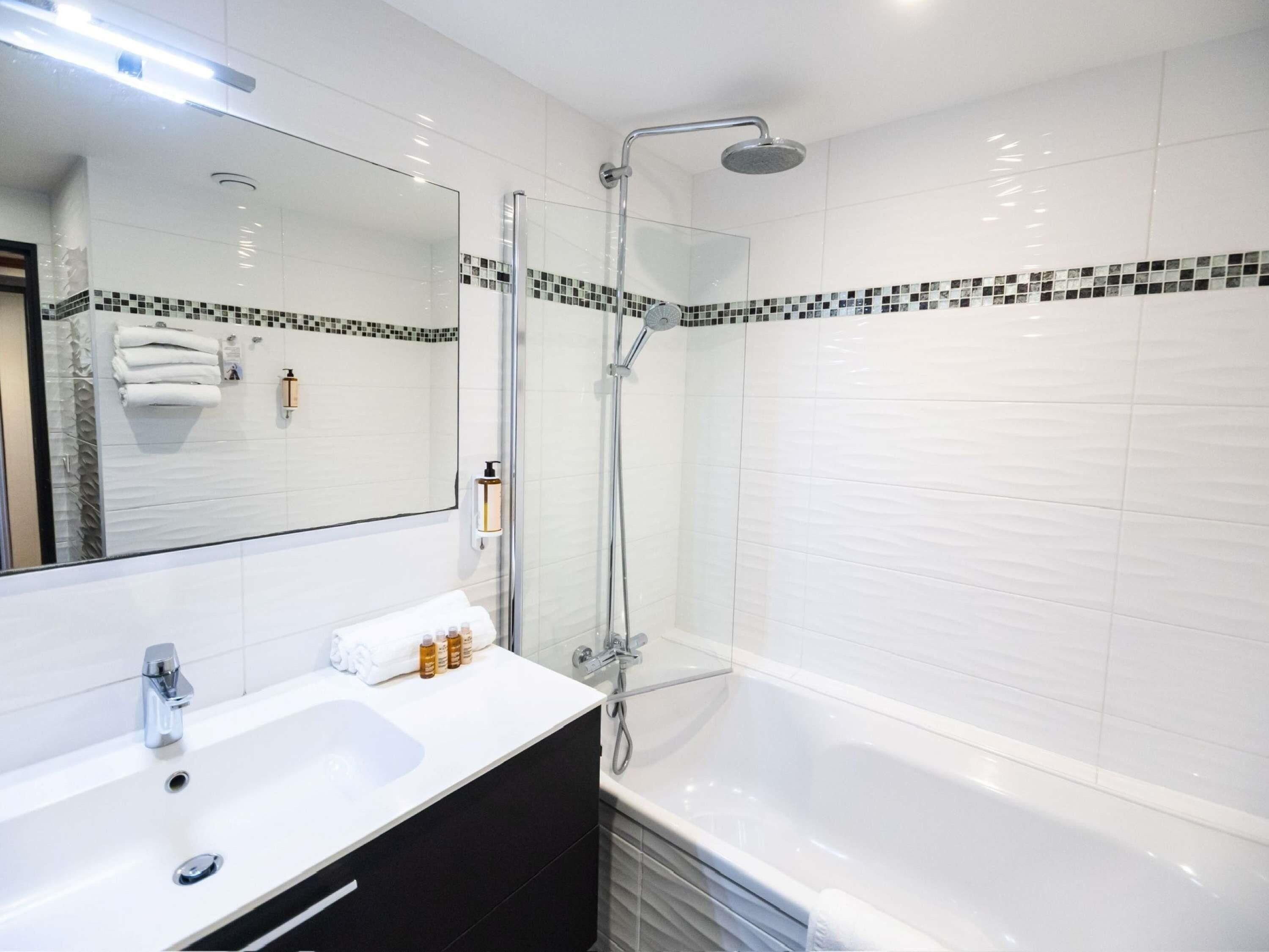 A modern bathroom with a white sink, a glass-enclosed shower, and a large mirror.