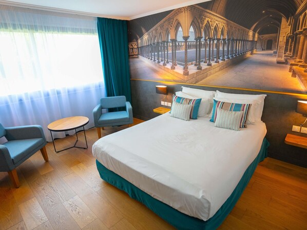 Une chambre d’hôtel avec un grand lit, une chaise, une petite table et une fresque représentant une cathédrale.