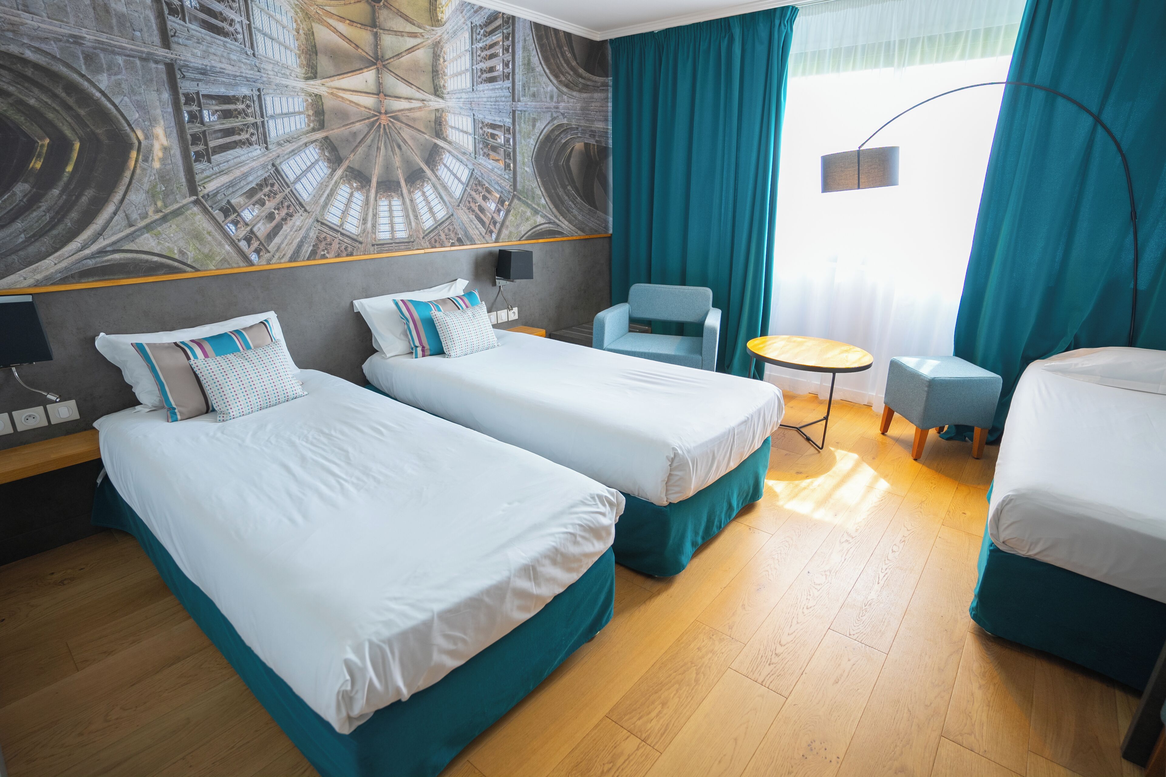 Een hotelkamer met twee bedden, een kleine tafel, een stoel en een groot raam met gordijnen.