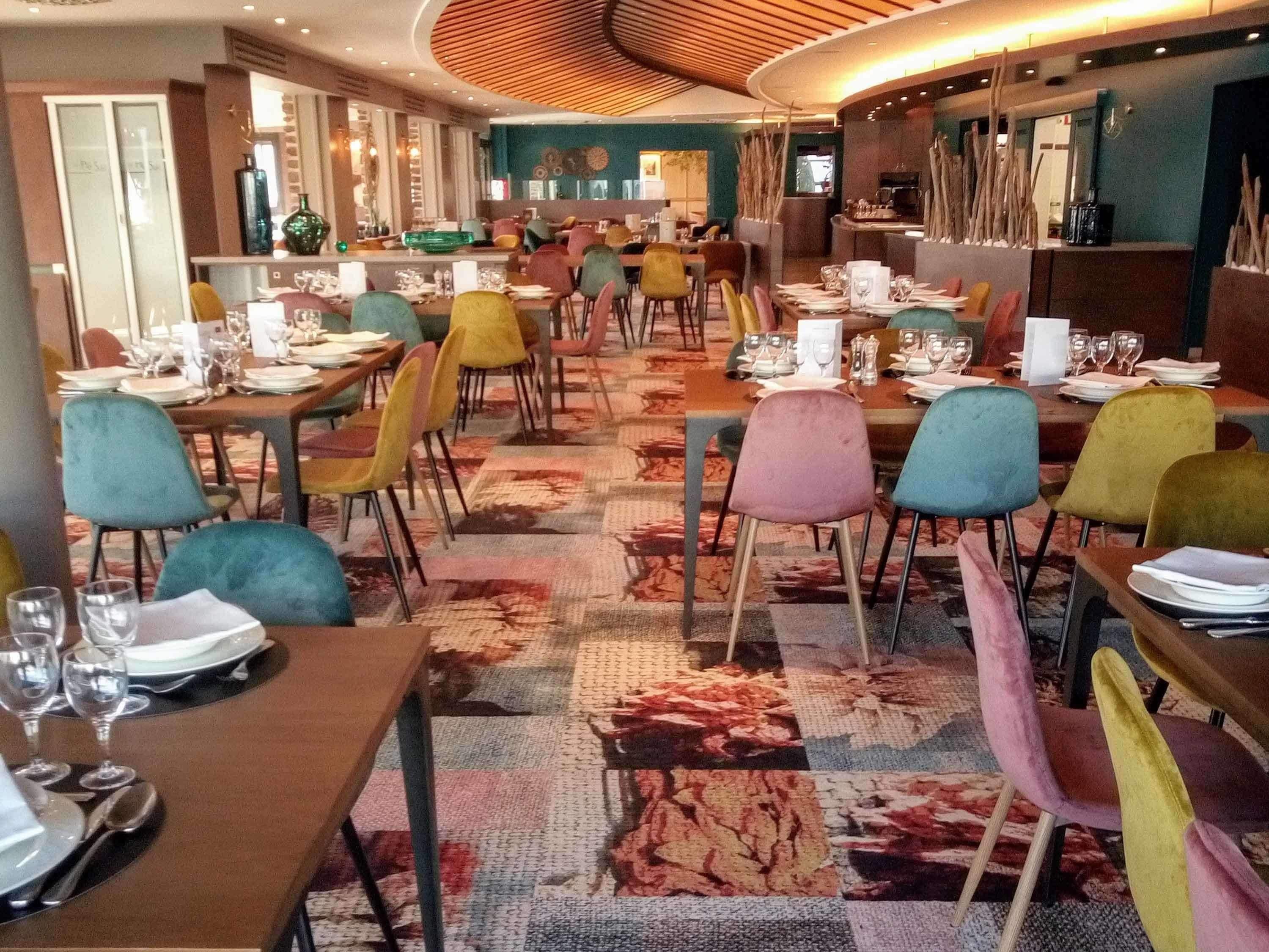 En restaurang med flera bord och stolar, en mönstrad matta och en modern takdesign.