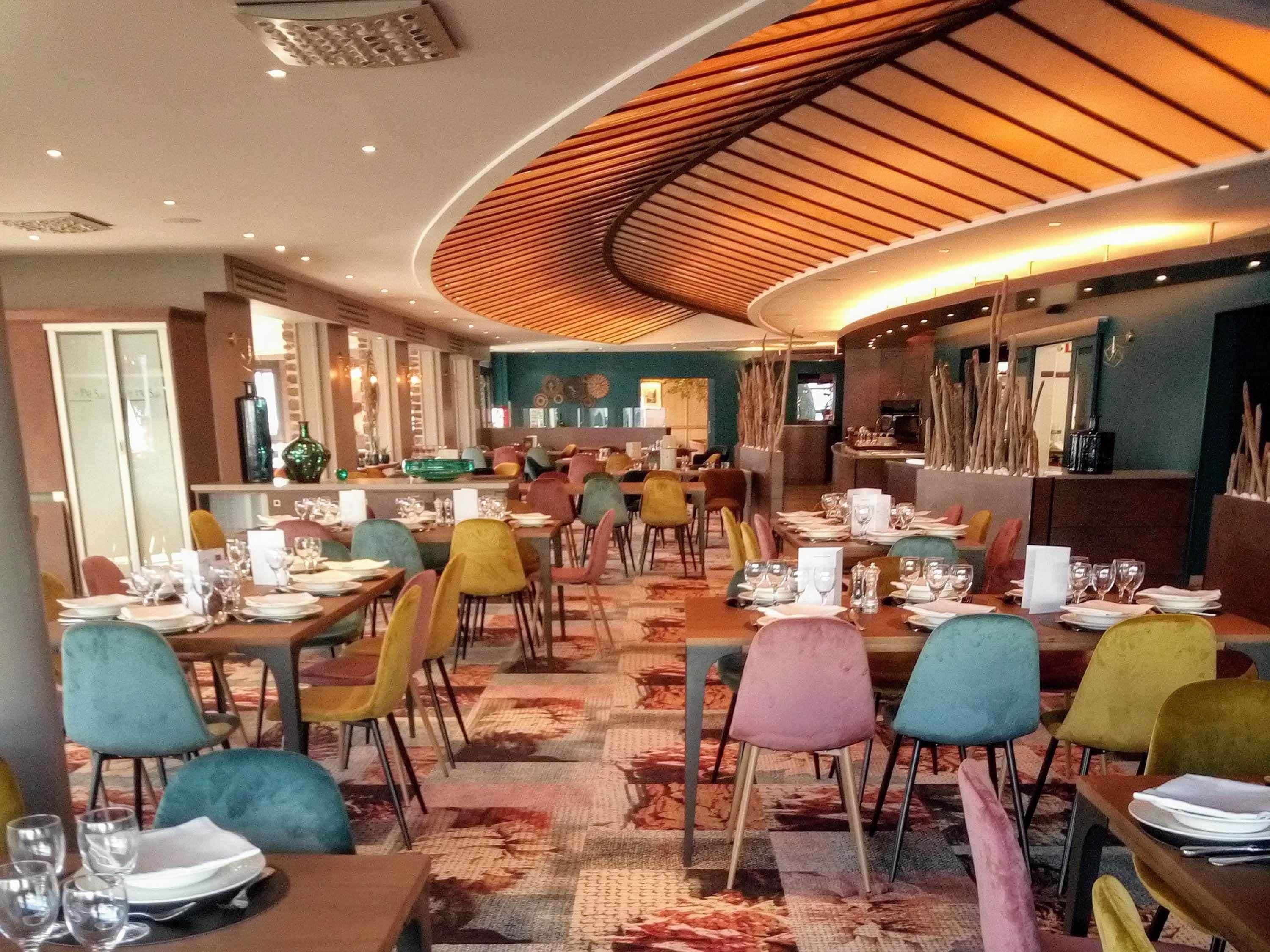 Ein Restaurant mit mehreren Tischen, bunten Stühlen und einem außergewöhnlichen Deckengestalt.