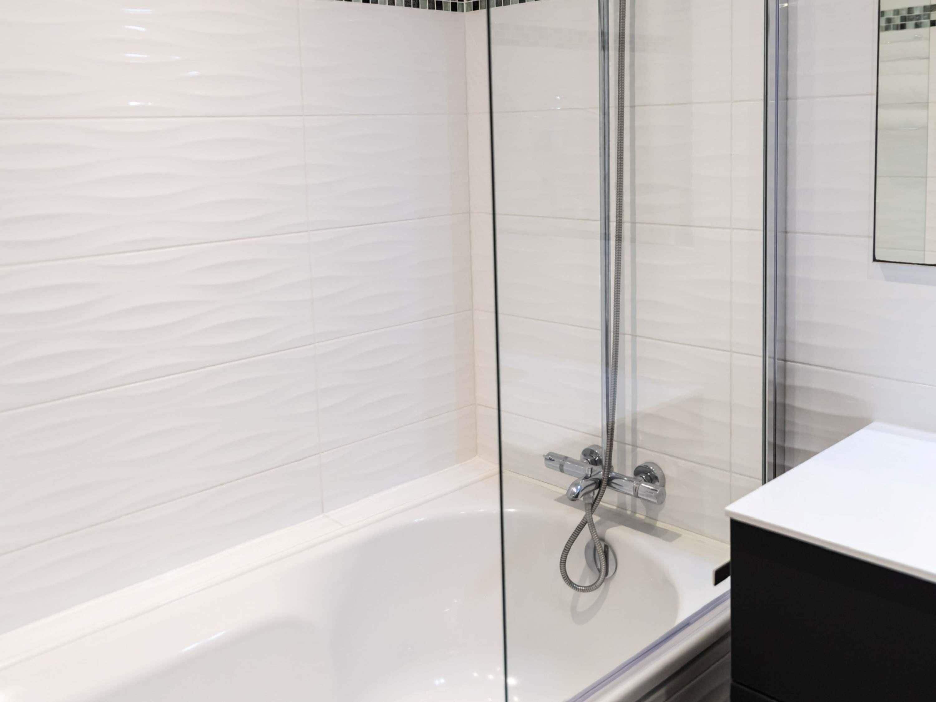 A modern bathroom with a glass-enclosed shower, a white bathtub, and a black vanity.