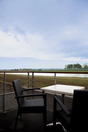 Un espace extérieur aménagé avec une table et des chaises, offrant une vue sur une étendue d’eau et un paysage lointain.