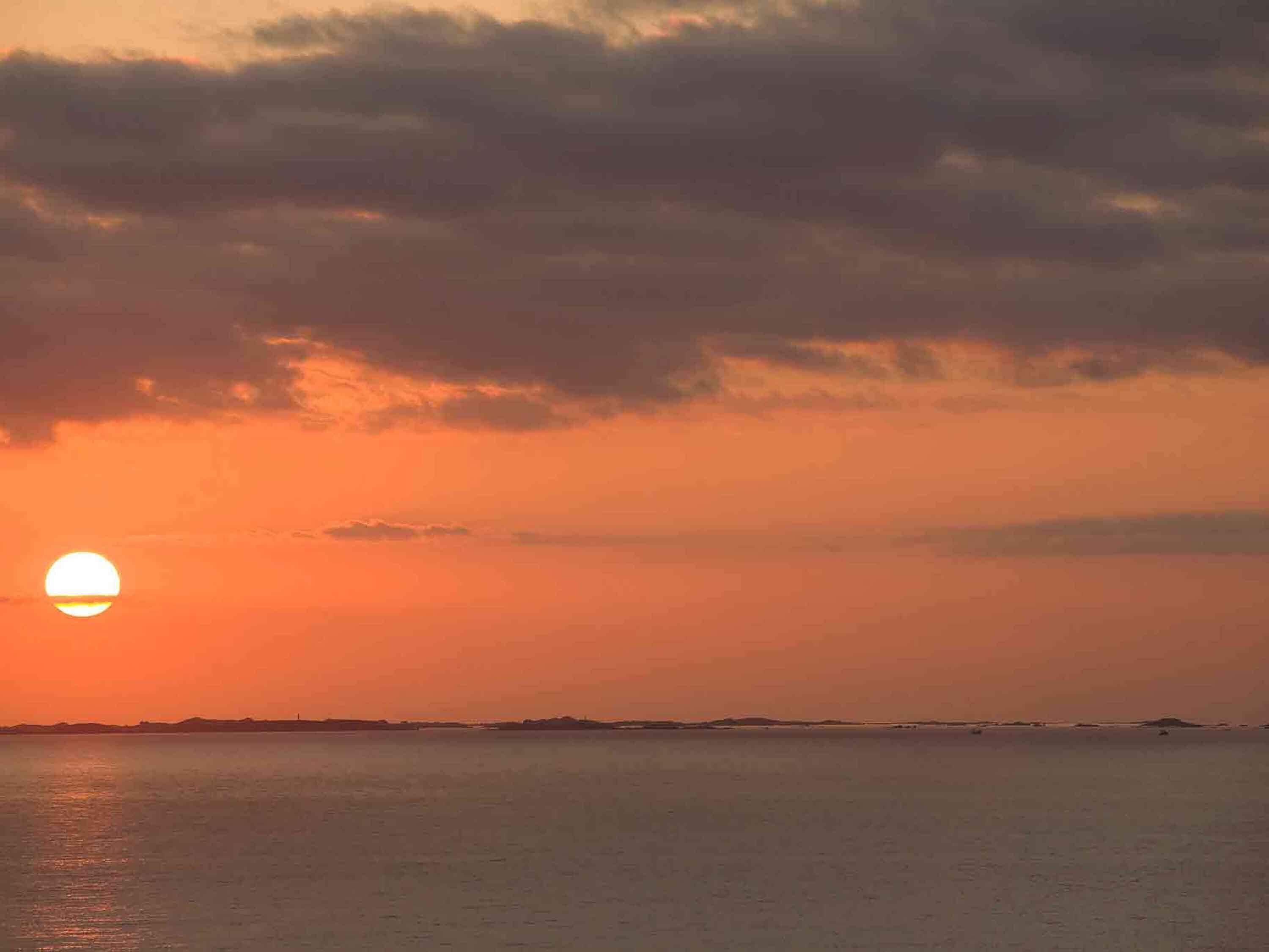 Un coucher de soleil sur une étendue d’eau, avec une côte lointaine à l’horizon.