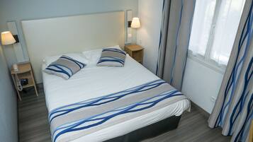 A neatly made bed with a striped bedspread, two bedside tables with lamps, a telephone, and a window with curtains.