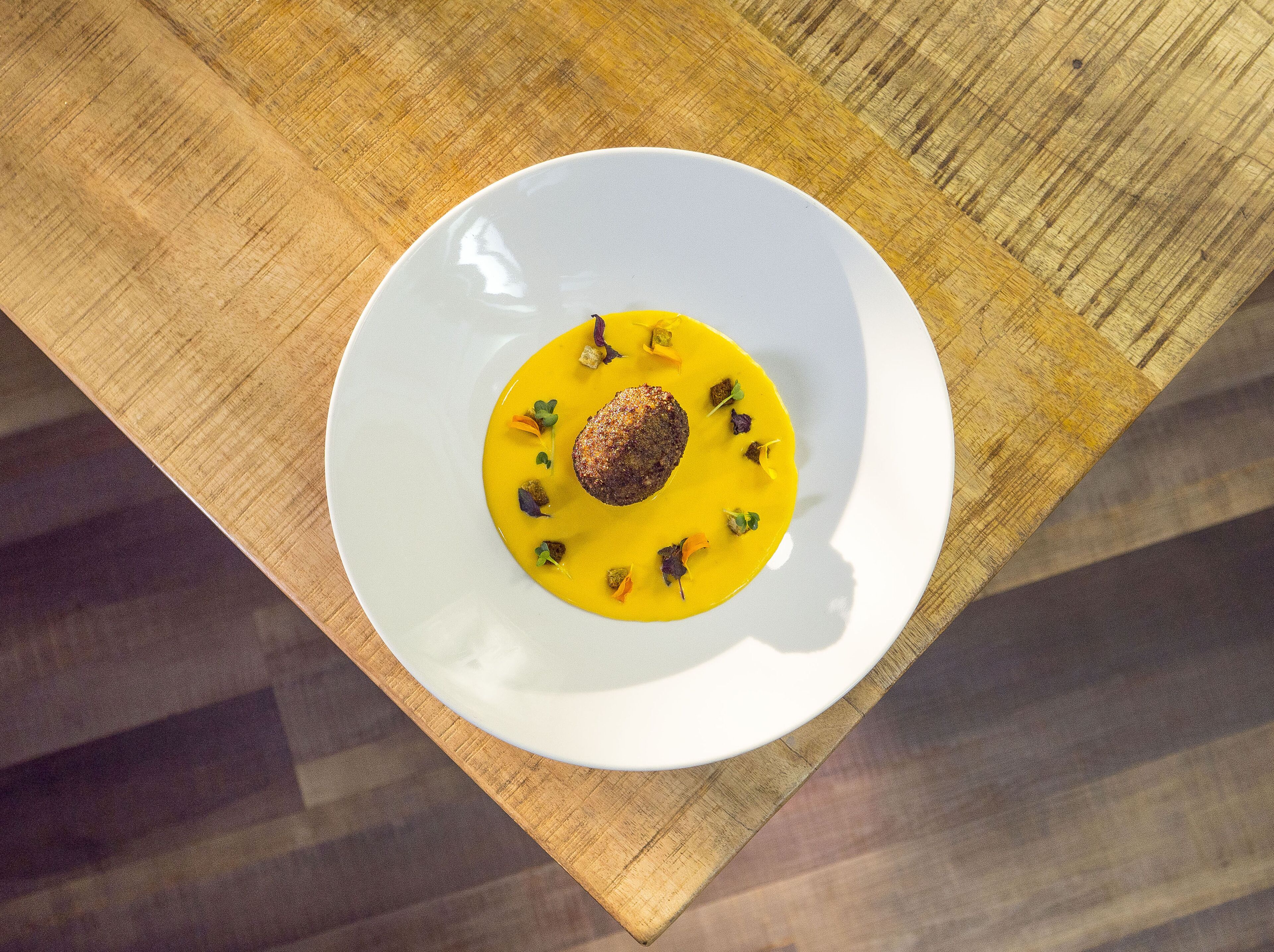 A white plate with a yellow sauce and a brown item, possibly a meat patty, on a wooden table.