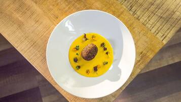 A white plate with a yellow sauce and a brown item, possibly a meat patty, on a wooden table.