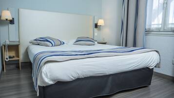 Ein modernes Hotelzimmer mit einem großen Bett, zwei Nachttischlampen, einem Nachttisch mit Telefon und einem Fenster mit Vorhängen.