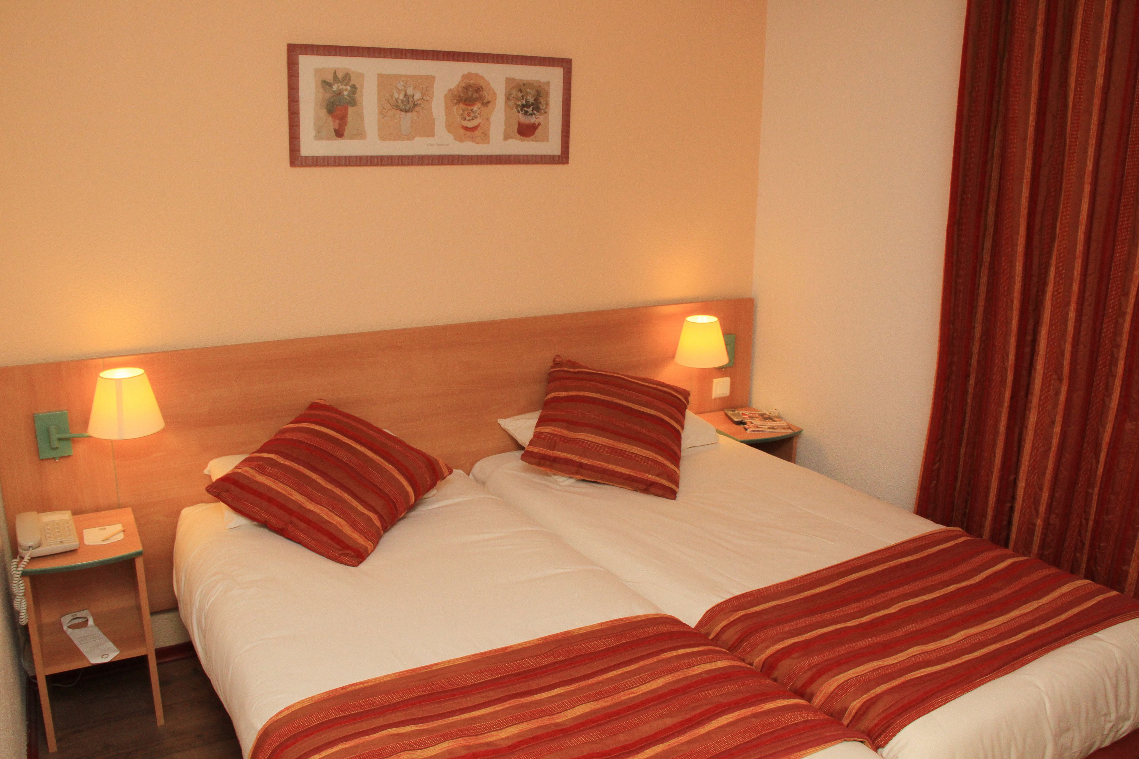 Ein Hotelzimmer mit einem großen Bett, zwei Nachttischlampen, einem Nachttisch mit Telefon und einem gerahmten Bild an der Wand.
