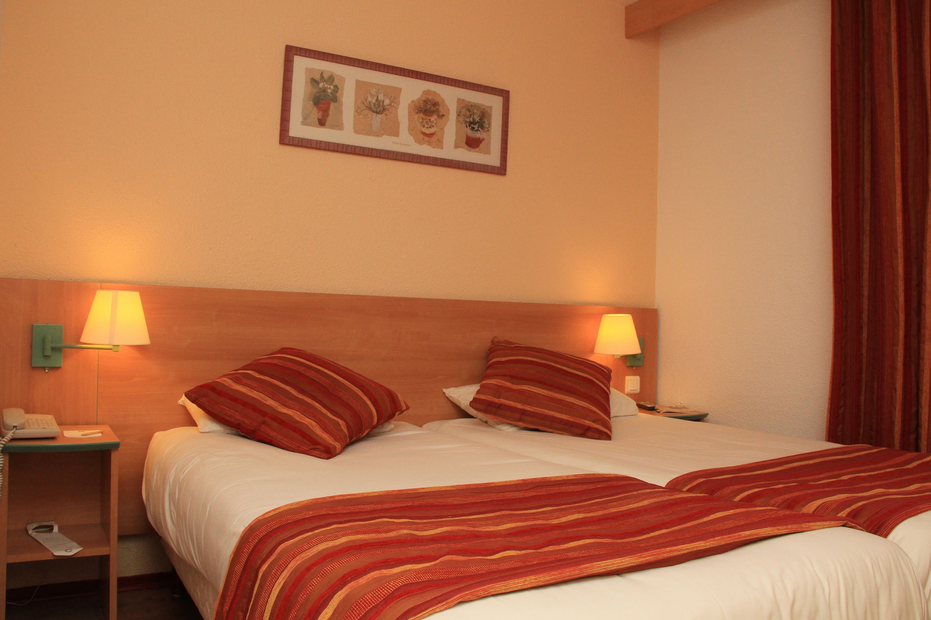 Habitación de hotel con cama, dos lámparas de noche, una mesita de noche y un cuadro en la pared.