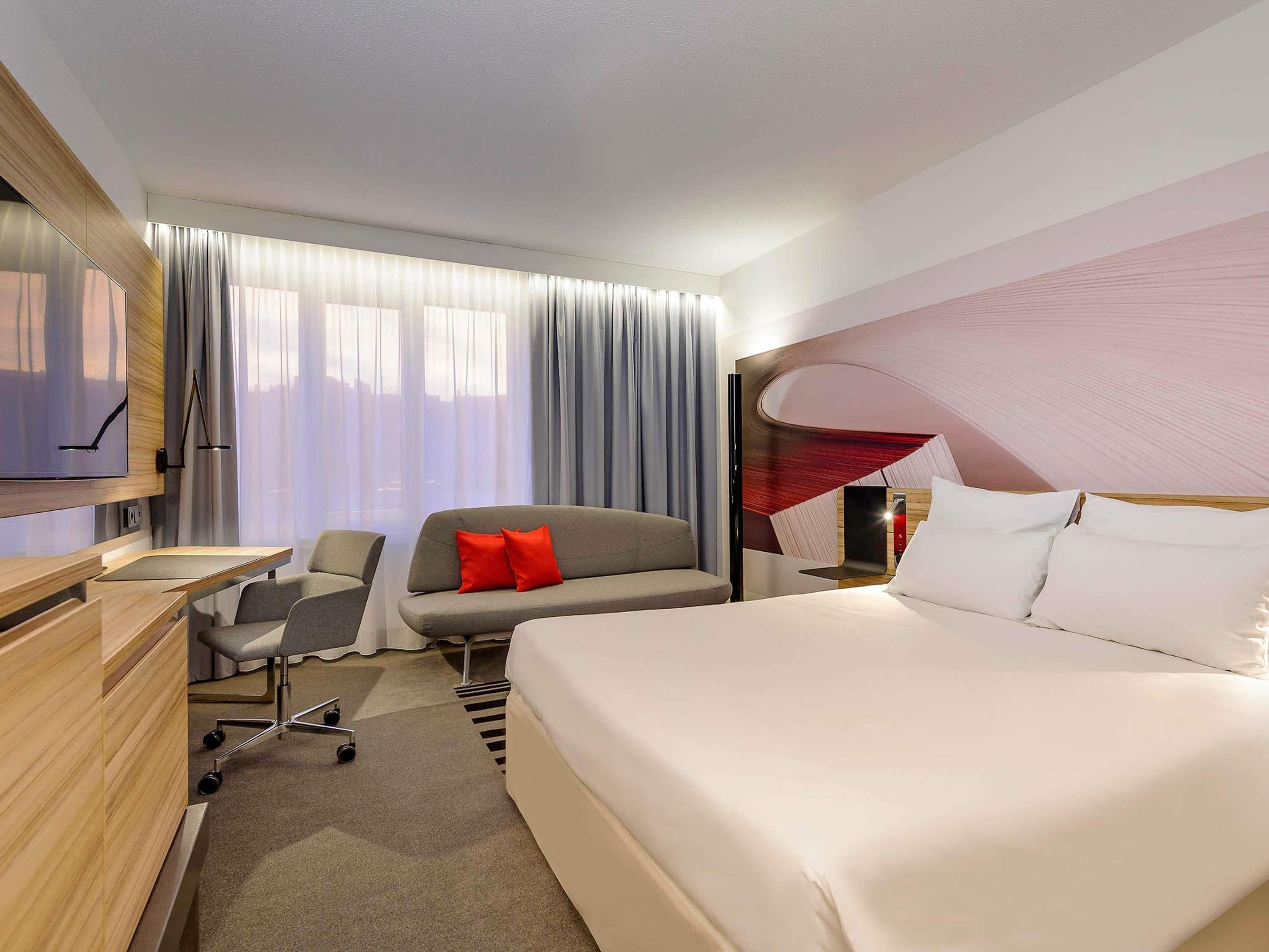 A modern hotel room with a large bed, a sofa, a desk, and a TV.
