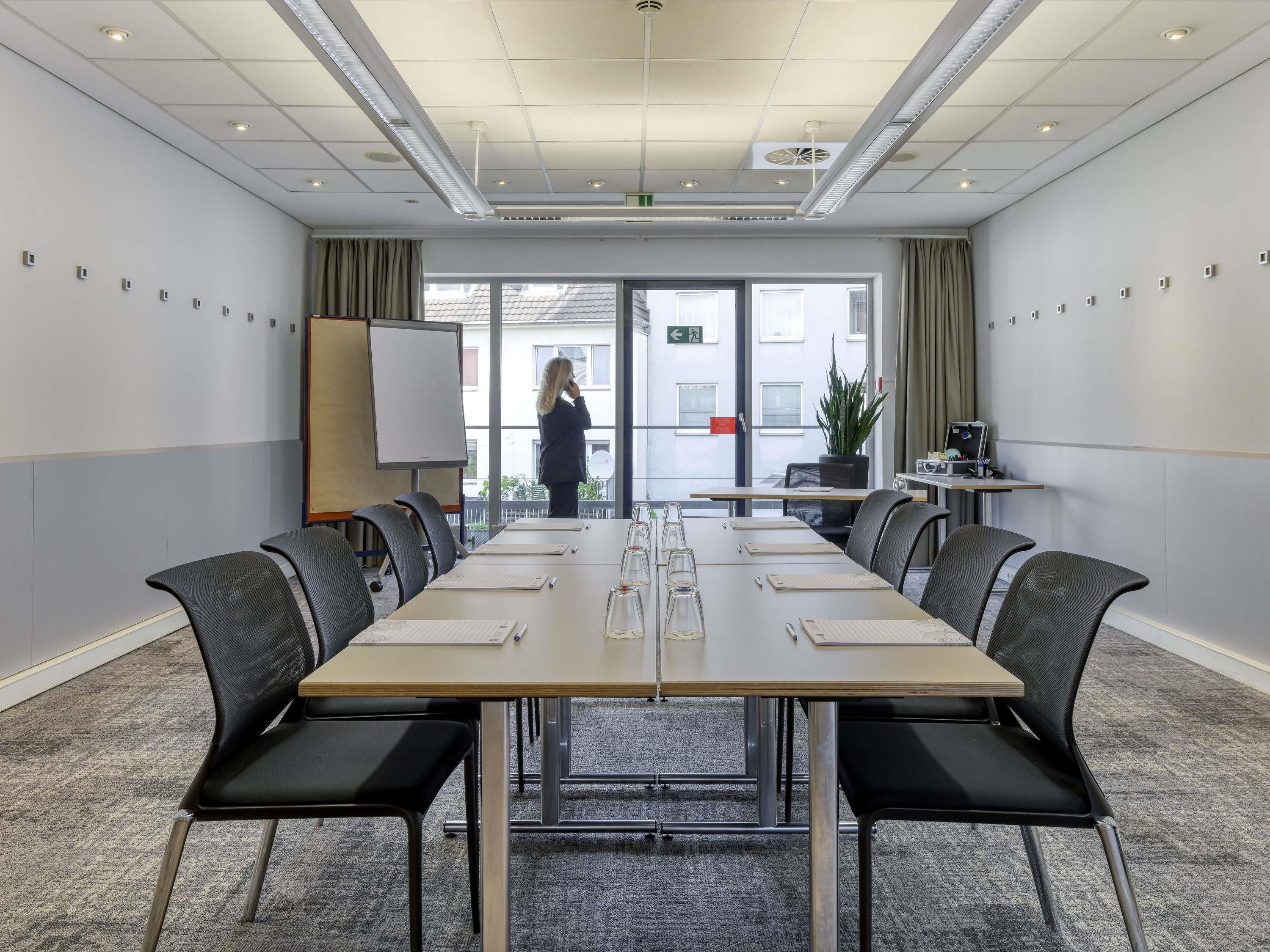 A conference room with a long table, chairs, a whiteboard, and a person standing by the door.