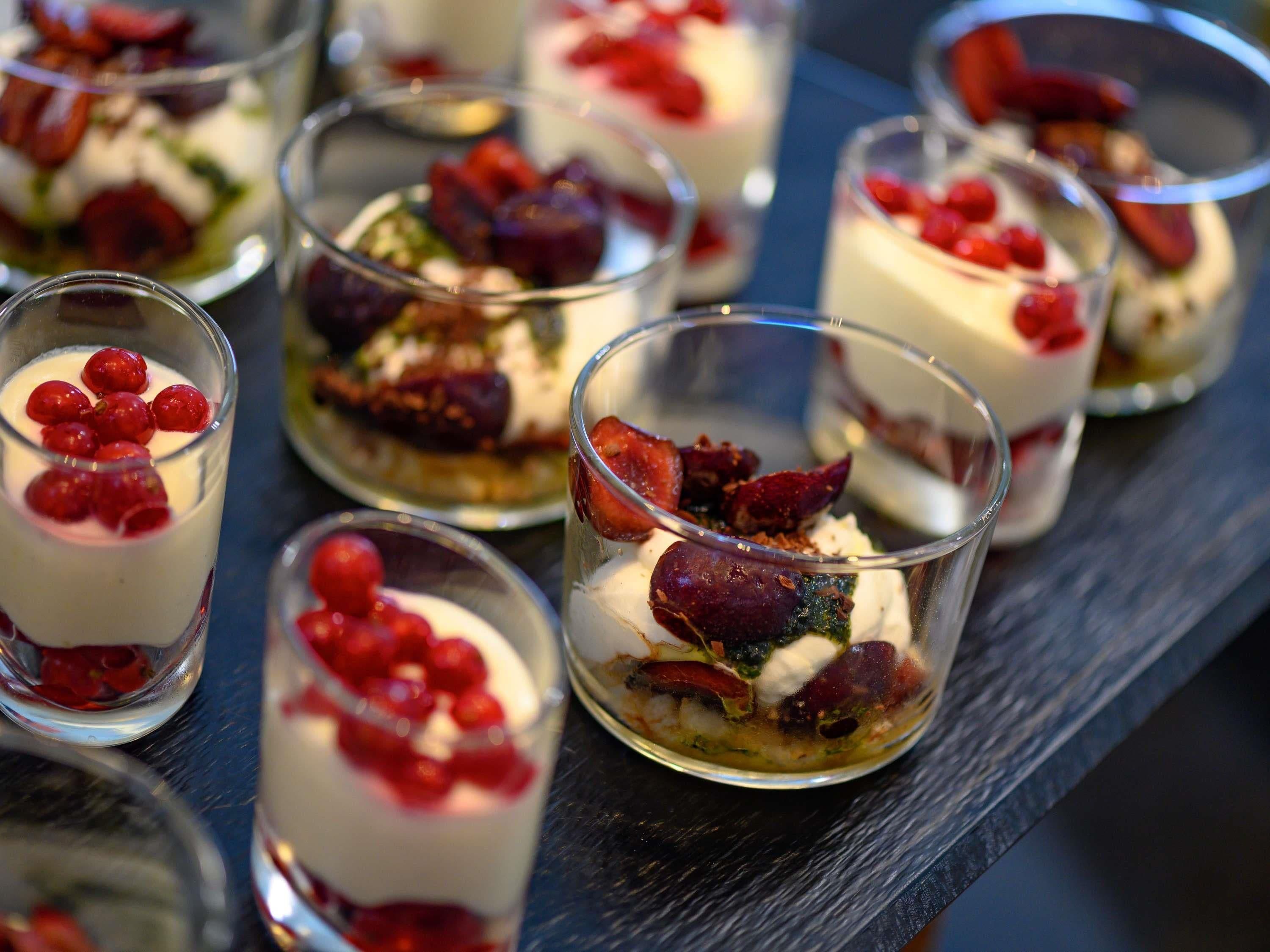 A series of dessert cups with layers of cream, berries, and what appears to be a crumble or crumble topping.