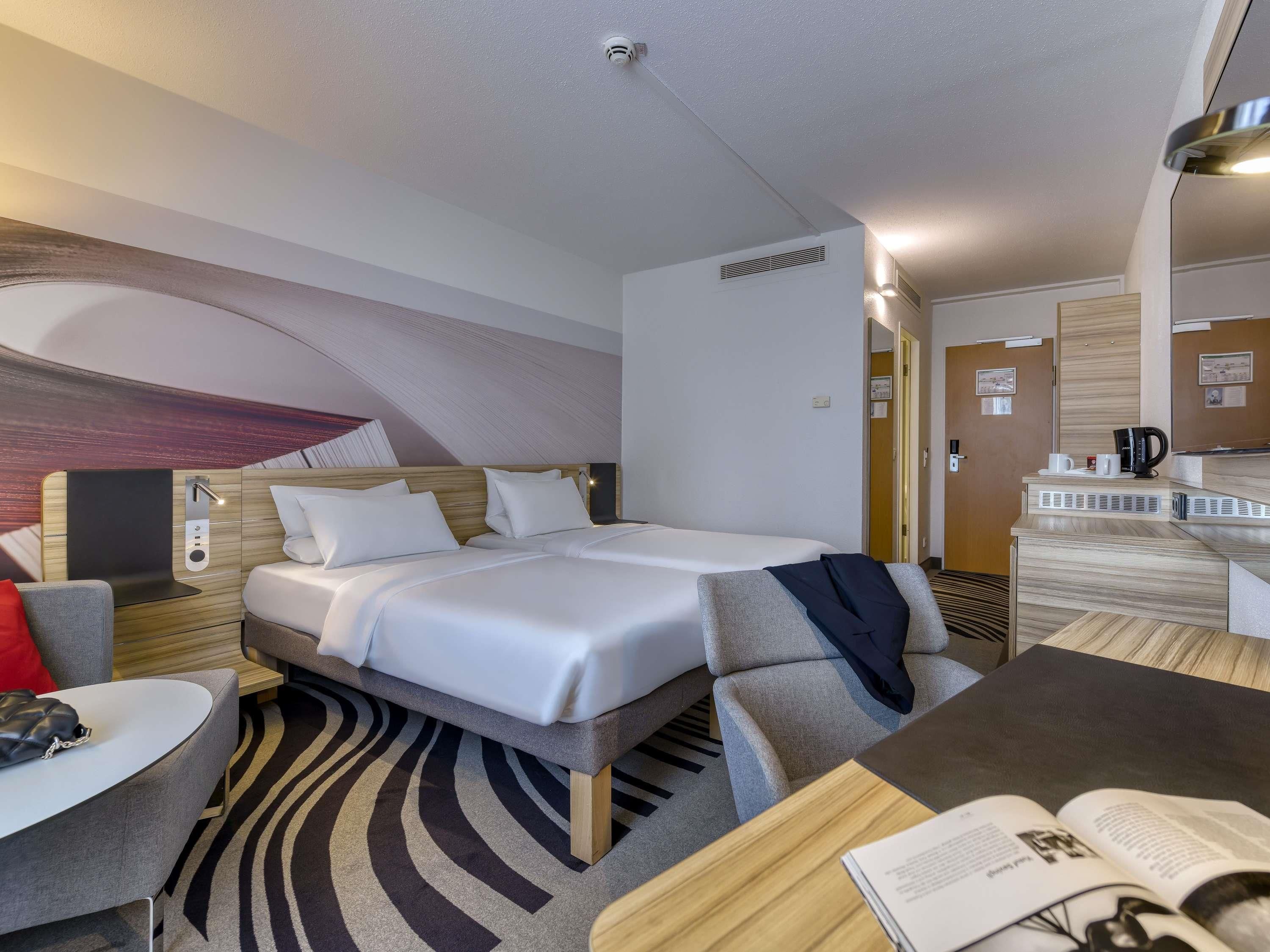 A modern hotel room with a bed, a desk, a chair, and a small table.