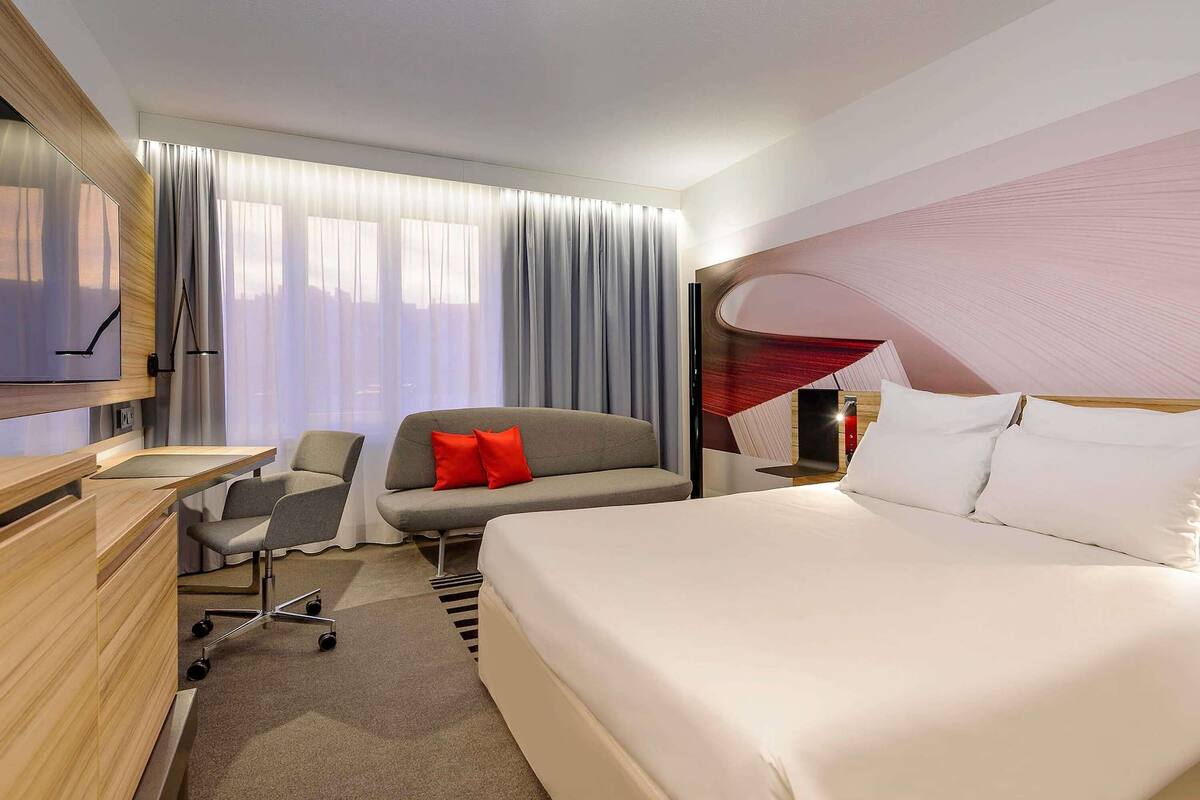 Moderni hotellihuone, jossa on suuri sänky, sohva, työpöytä ja televisio.