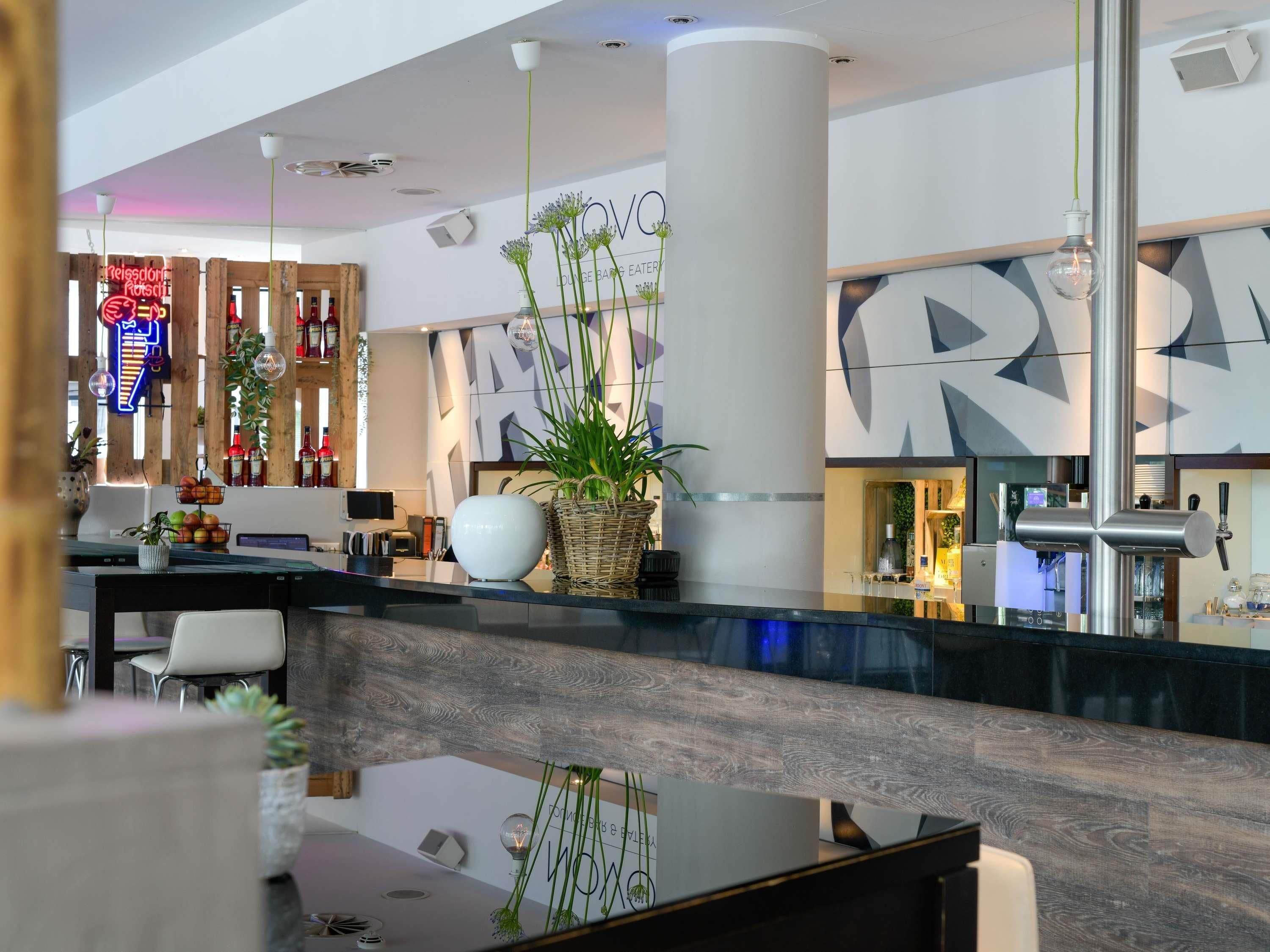 A modern hotel lobby with a reception desk, seating area, and a bar.