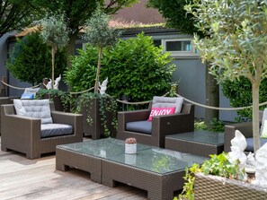 Un espace extérieur aménagé avec des meubles en osier, une table à plateau en verre et de la verdure.