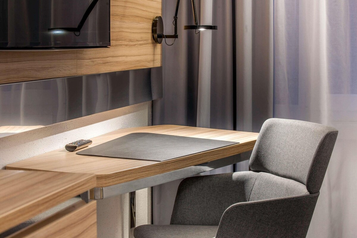 A modern room with a wooden desk, a grey chair, a mounted TV, and a pendant light.