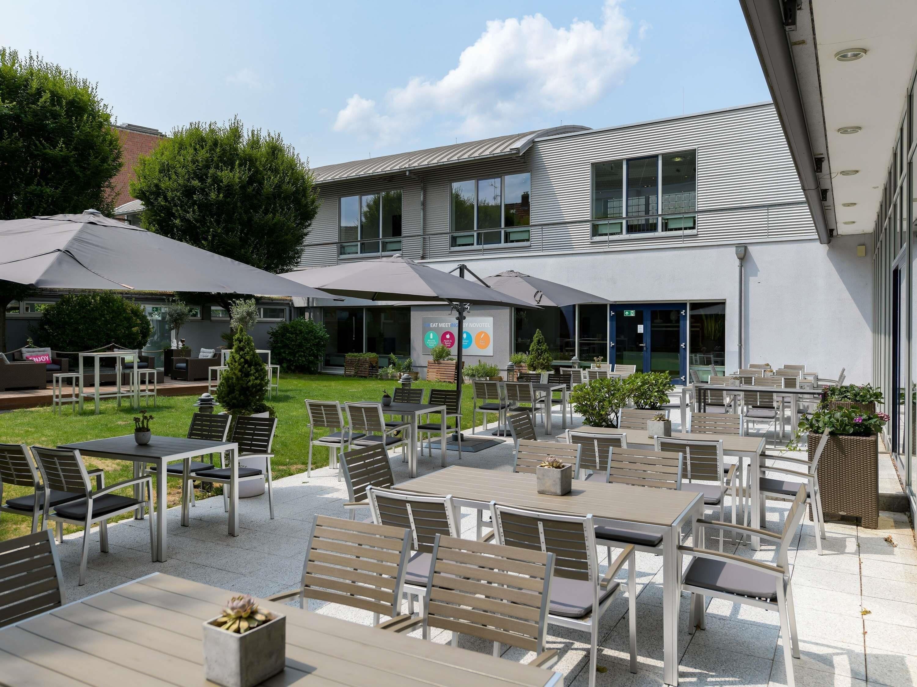 An outdoor patio area with tables and chairs, a sign for 'EAT MEAT', and a building with large windows in the background.