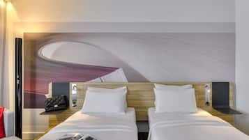 Quarto de hotel com duas camas, um grande mural abstrato na parede, uma mesinha com uma bolsa e uma revista na cama.