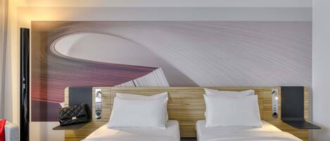 A hotel room with two beds, a large abstract mural on the wall, a small table with a handbag, and a magazine on the bed.