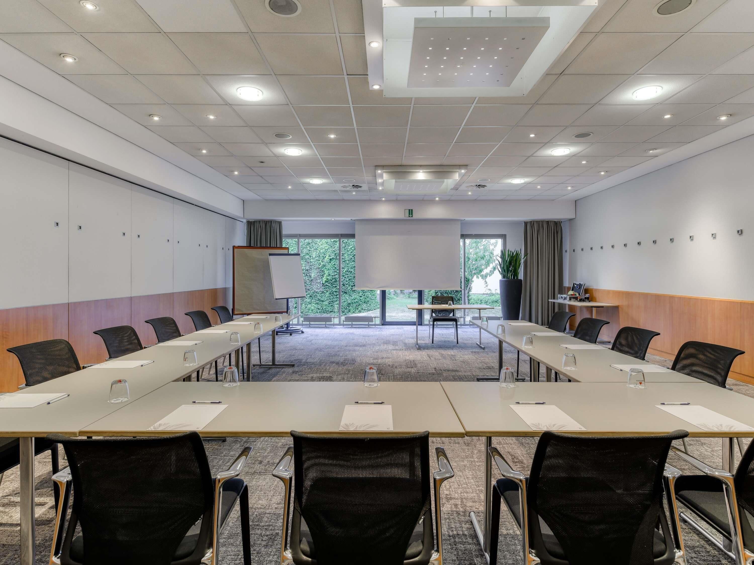 A conference room with a long table, chairs, a whiteboard, and a projector screen.