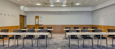 A conference room with tables, chairs, a clock, and a projector screen.
