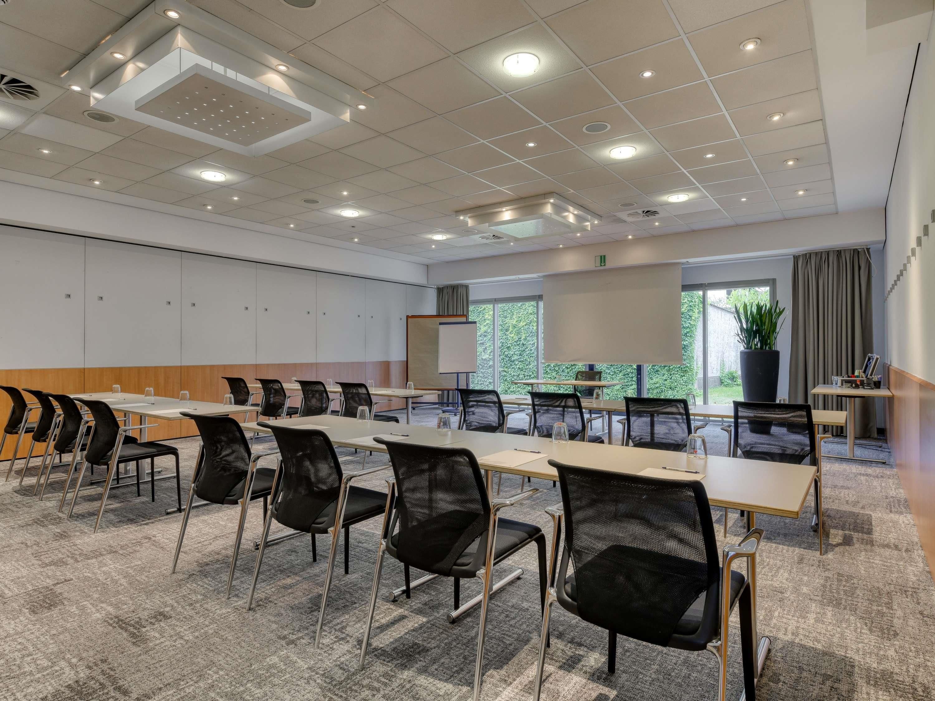 Une salle de conférence équipée d’une longue table, de chaises, d’un écran de projection et d’une grande fenêtre donnant sur un paysage verdoyant.