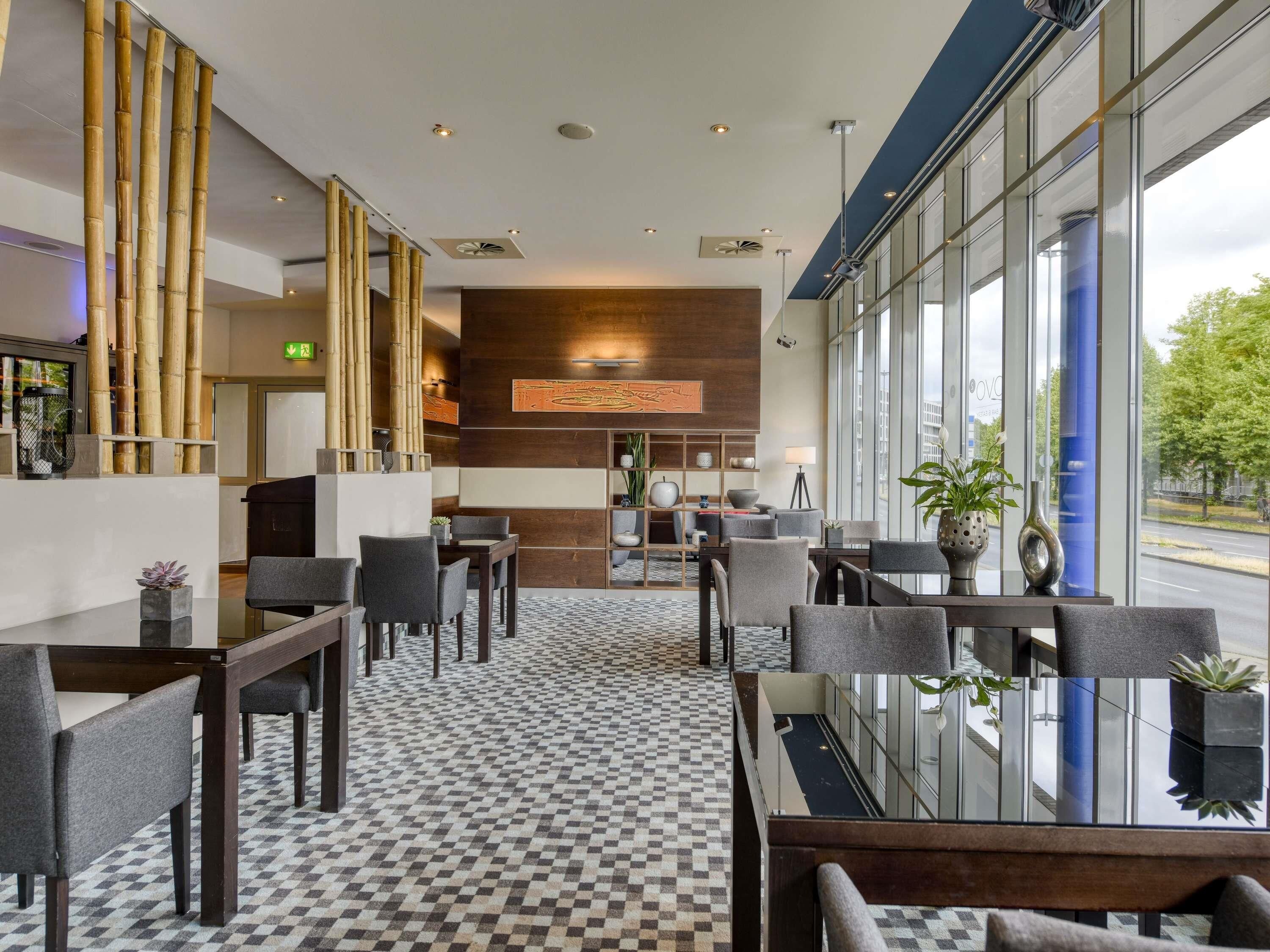 A hotel lobby with checkered flooring, seating arrangements, and large windows offering a view of the street.