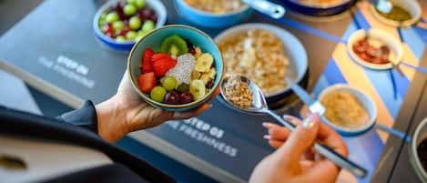 A person holding a bowl of fruit and yogurt, with various other food items and bowls on a tray.