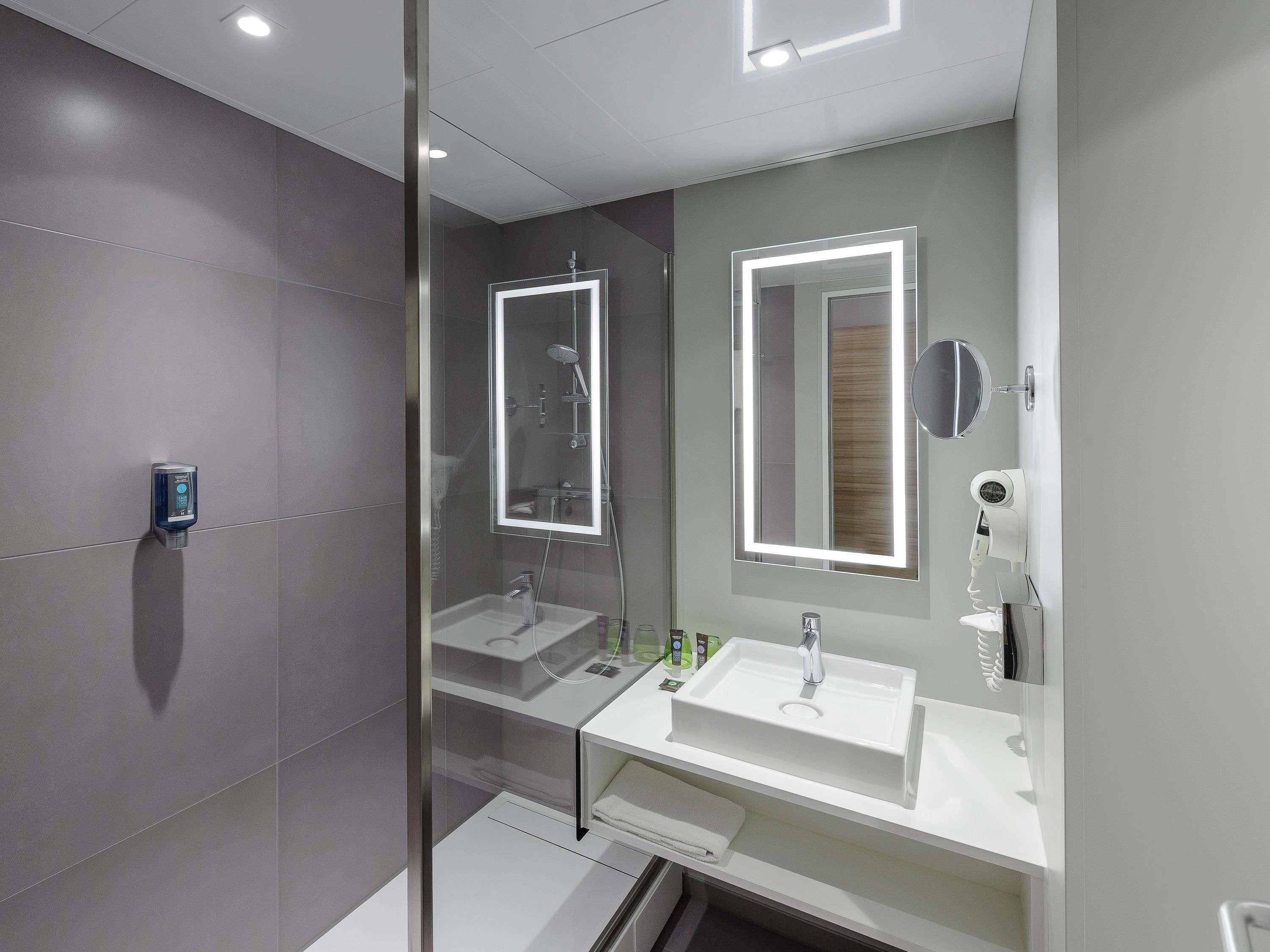 A modern bathroom with a glass-enclosed shower, two sinks, and a mirror with integrated lighting.
