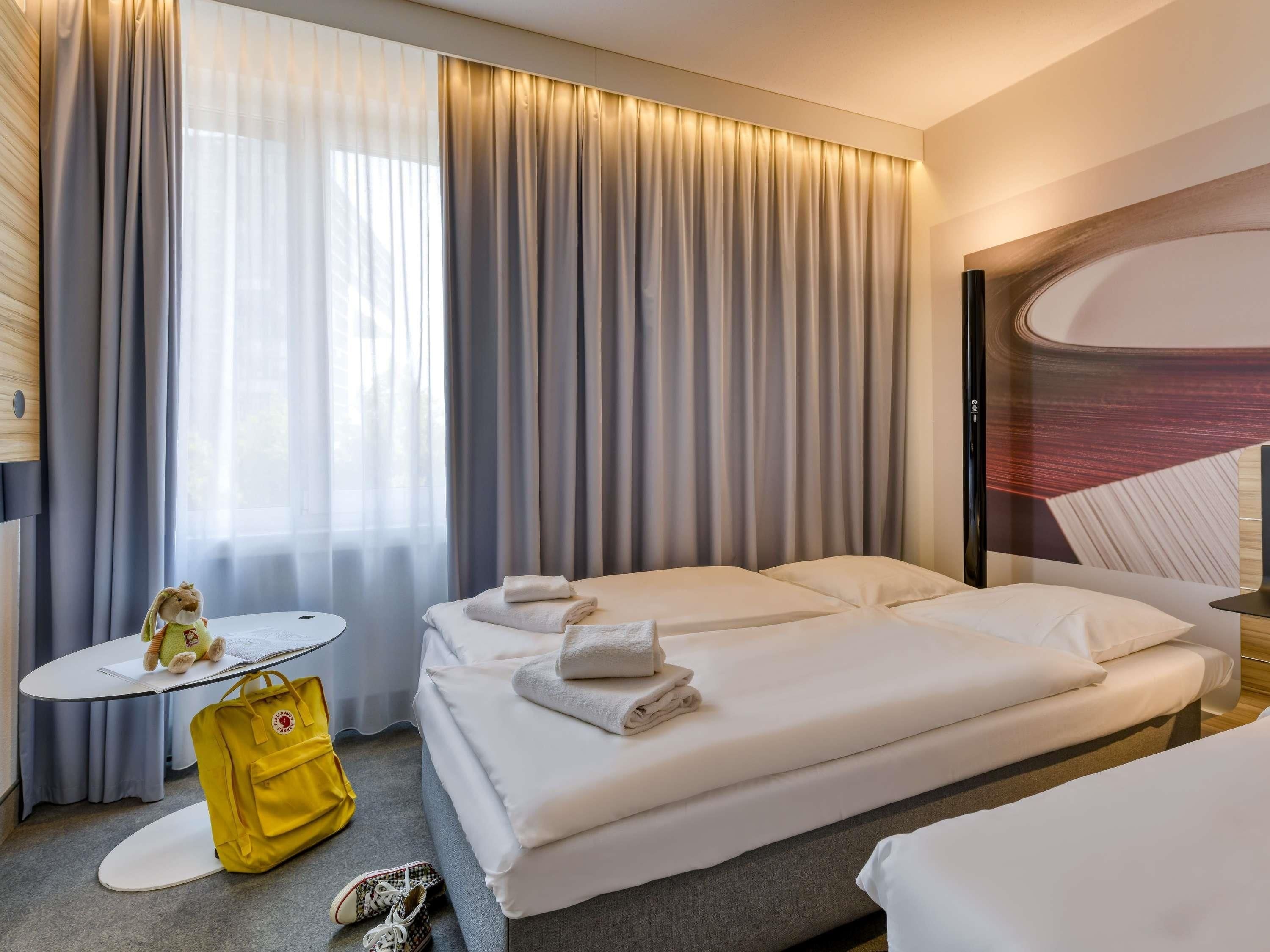 A hotel room with two beds, a small table, a yellow bag, and a pair of shoes.