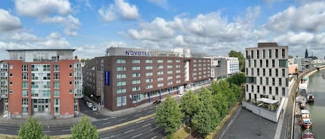 A Novotel hotel with a modern brick facade, located near a river with boats docked.